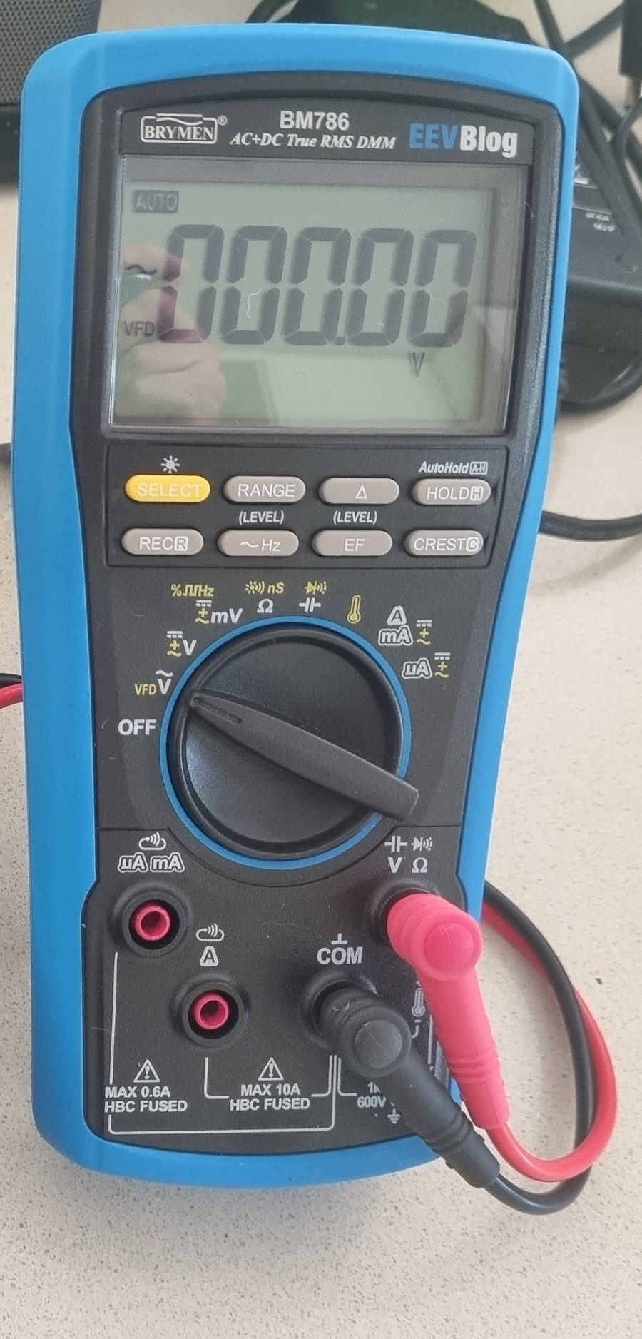 The EEVblog BM786 multimeter on a bench: the display shows the AC and VFD symbols and reads 000.00 volts, with the yellow SELECT button, the other seven grey buttons, the rotary dial and four input jacks below