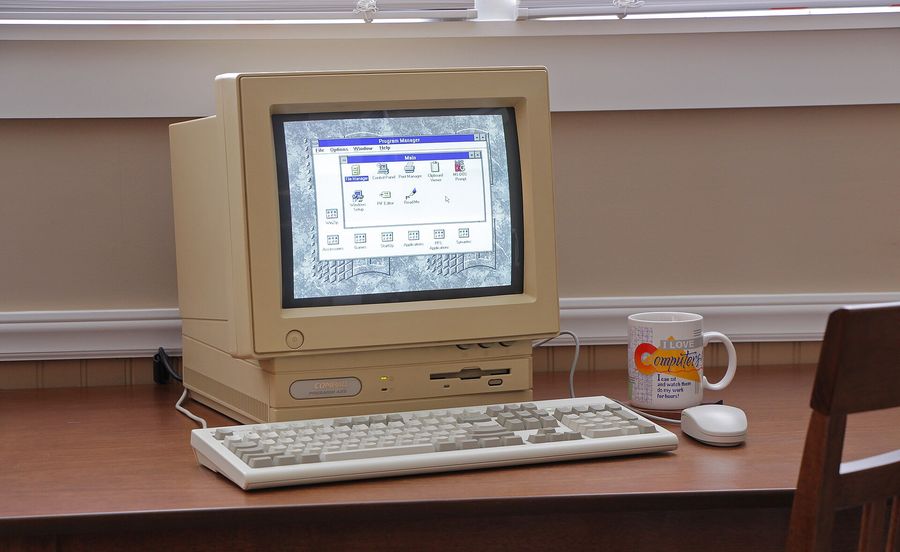 A beige 1990s Compaq Presario all-in-one computer on a wooden desk, its screen showing the Windows 3.1 Program Manager, with a keyboard and mouse in front