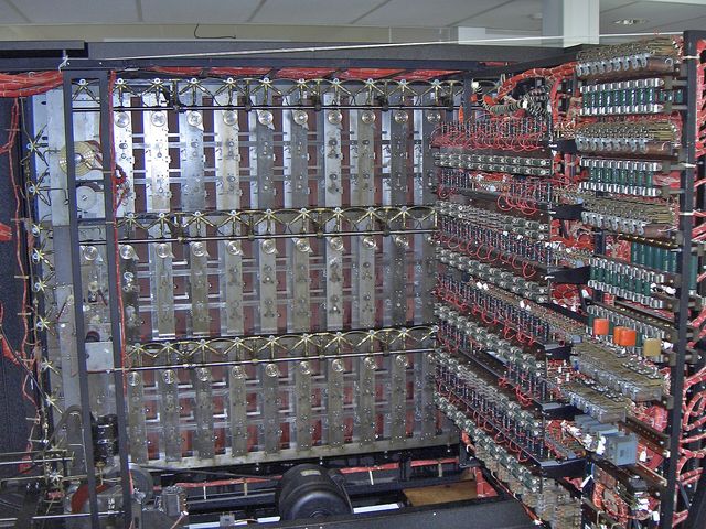 The back of a large cabinet packed with rows of rotating drums and red wiring