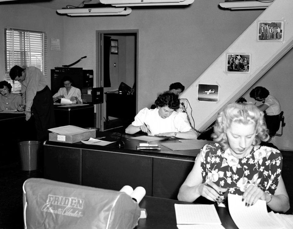 Women at desks in a 1949 office, working through paper records with slide rules and a mechanical calculator