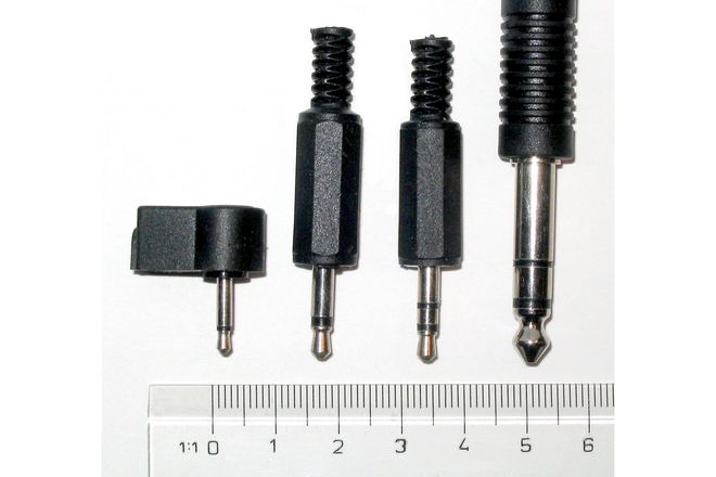 Four phone plugs beside a ruler: 2.5 mm, 3.5 mm mono, 3.5 mm stereo and 6.35 mm