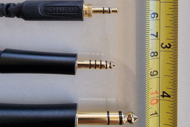 A 3.5 mm plug, a five-contact 4.4 mm balanced plug and a 6.35 mm plug beside a tape measure