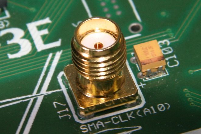 An SMA socket on a circuit board: a gold threaded barrel with a white insulator and a centre hole