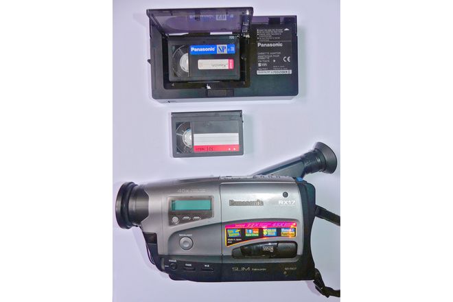A VHS-C camcorder, a small VHS-C tape and the full-size adapter it fits into